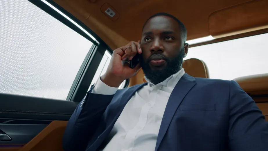 A passenger in a suit on the phone in the back of a sedan with leather seats