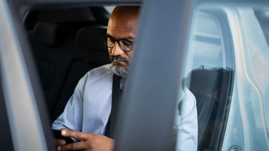 Un passager consulte son téléphone à l'arrière d'une voiture, vu par la portière ouverte