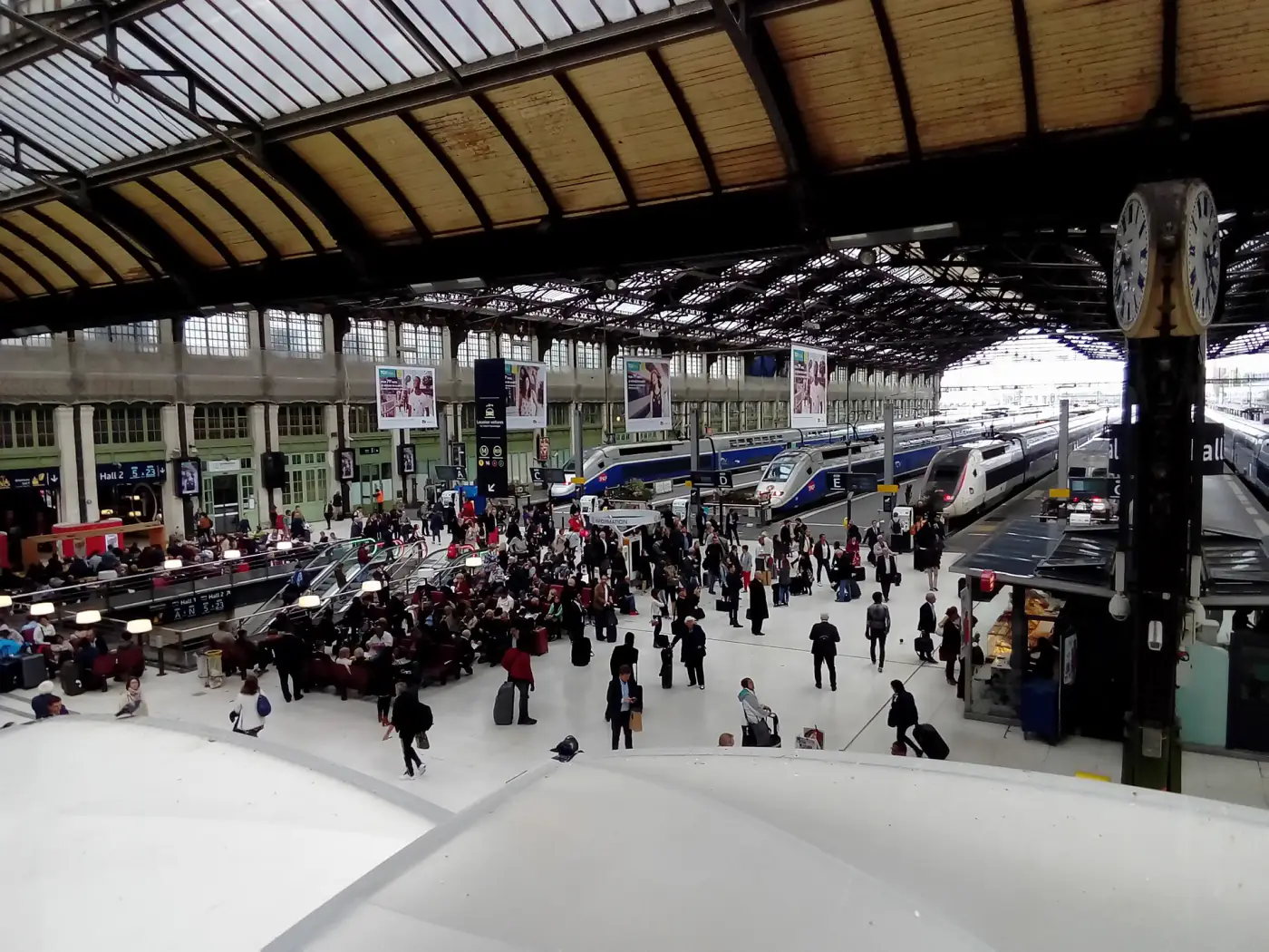 Travellers in Hall 1 of Gare de Lyon in Paris, under the glass roof, with TGV trains along the platforms.