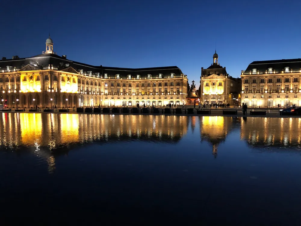 La place de la Bourse illuminée à la tombée de la nuit, reflétée dans le miroir d'eau de Bordeaux